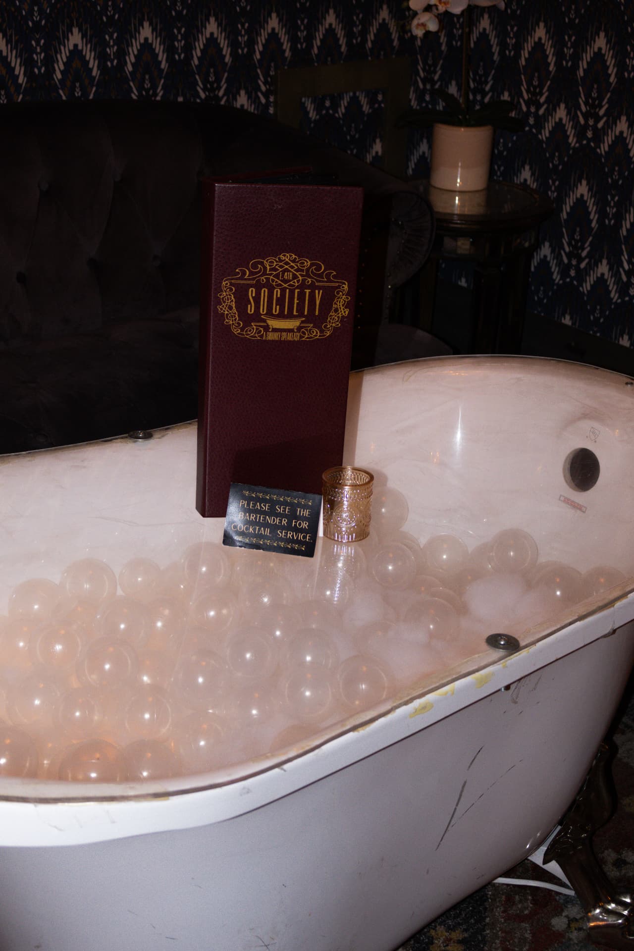 Society's vintage bathtub filled with translucent bubbles, with a Society menu and candle on top