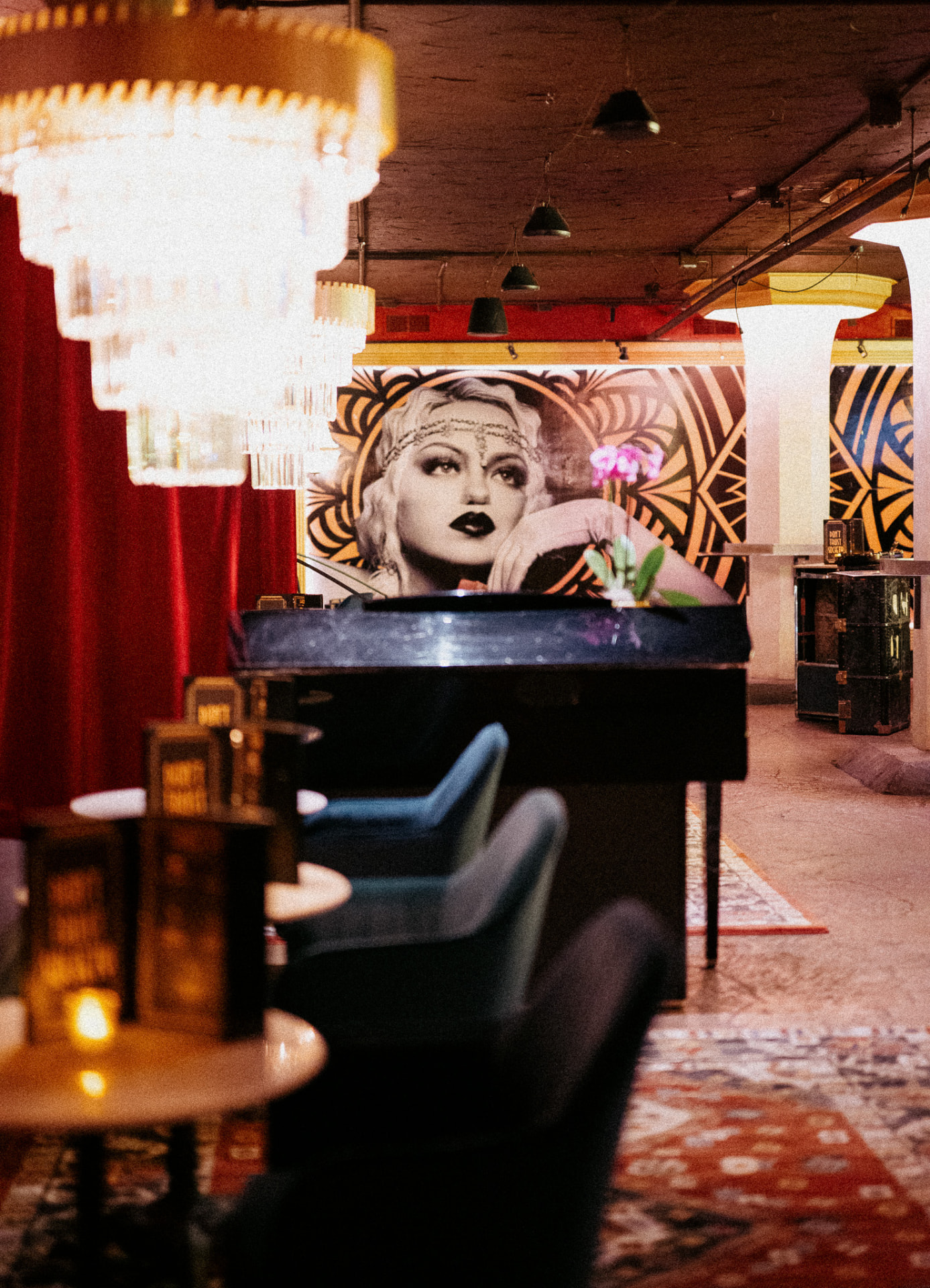 Society's speakeasy with crystal chandeliers, red velvet curtains and a deco flapper mural