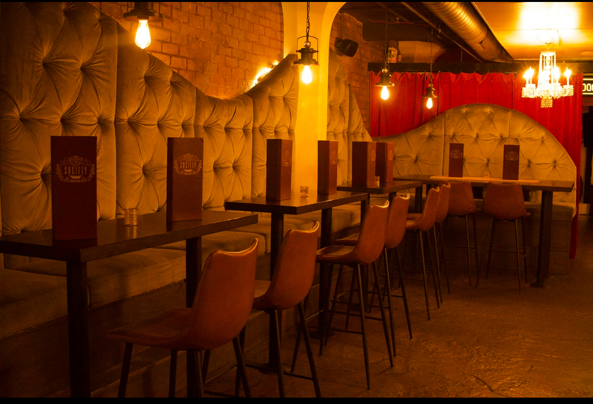 Society's tufted velvet banquette with high-top tables, leather bar stools and Edison bulb pendants