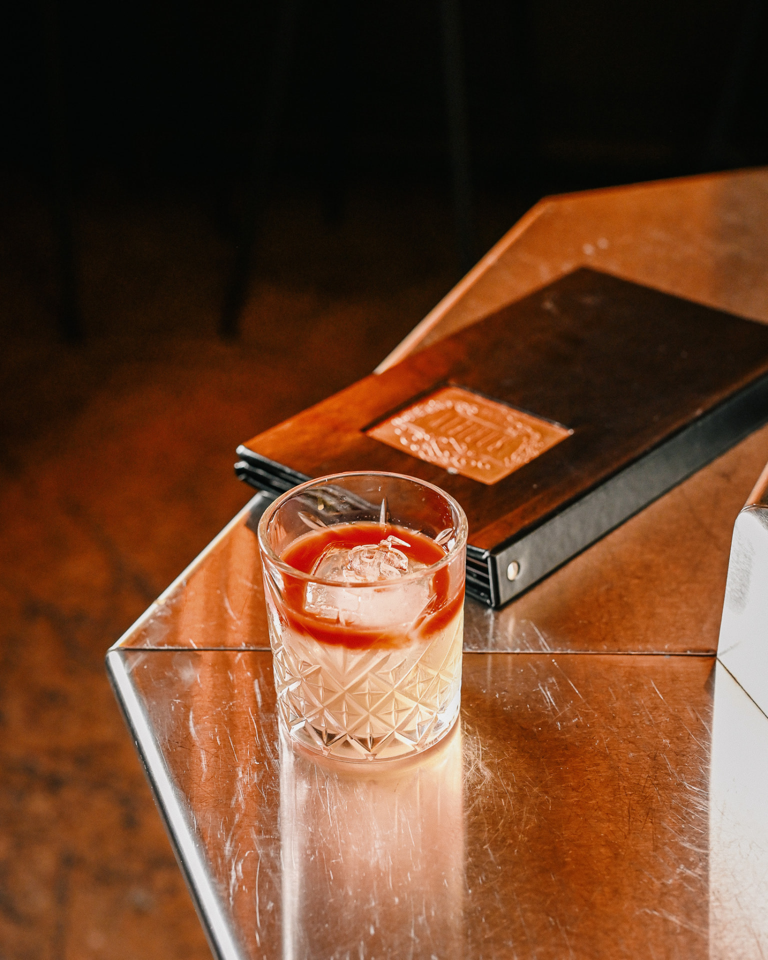 A cut-crystal cocktail beside a leather menu on a brass table