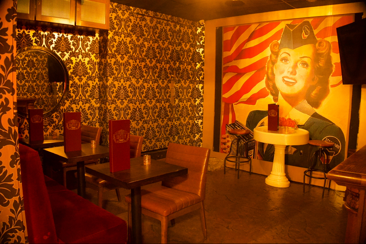 The Boom Boom Room with damask wallpaper, red velvet banquette, a vintage pin-up mural and a pedestal sink table